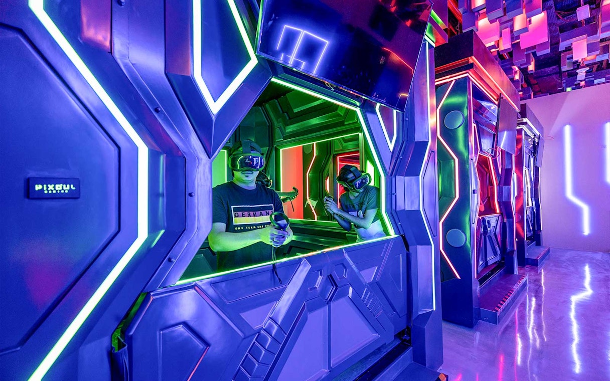 Visitors engaging in a VR game at Pixoul Gaming with neon-lit futuristic booths.