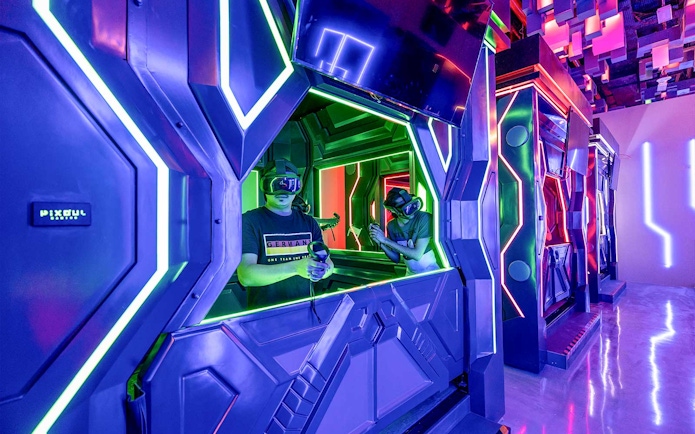 Visitors engaging in a VR game at Pixoul Gaming with neon-lit futuristic booths.