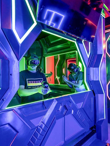 Visitors engaging in a VR game at Pixoul Gaming with neon-lit futuristic booths.