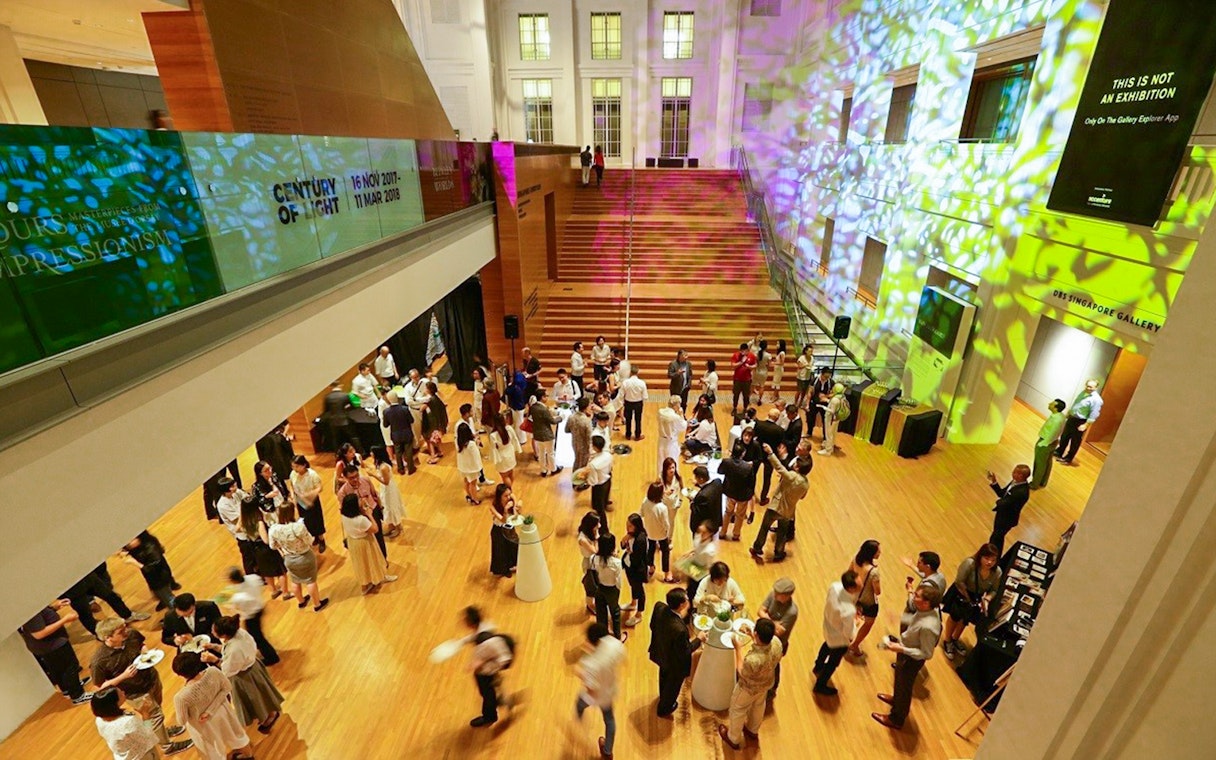 Visitors at National Gallery Singapore event in a brightly lit hall with colorful projections.