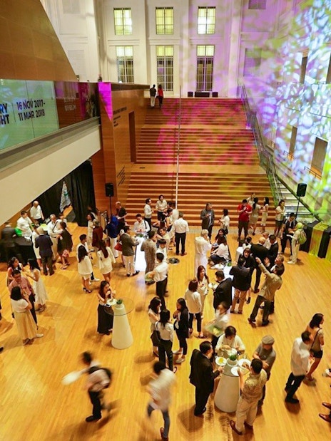 Visitors at National Gallery Singapore event in a brightly lit hall with colorful projections.