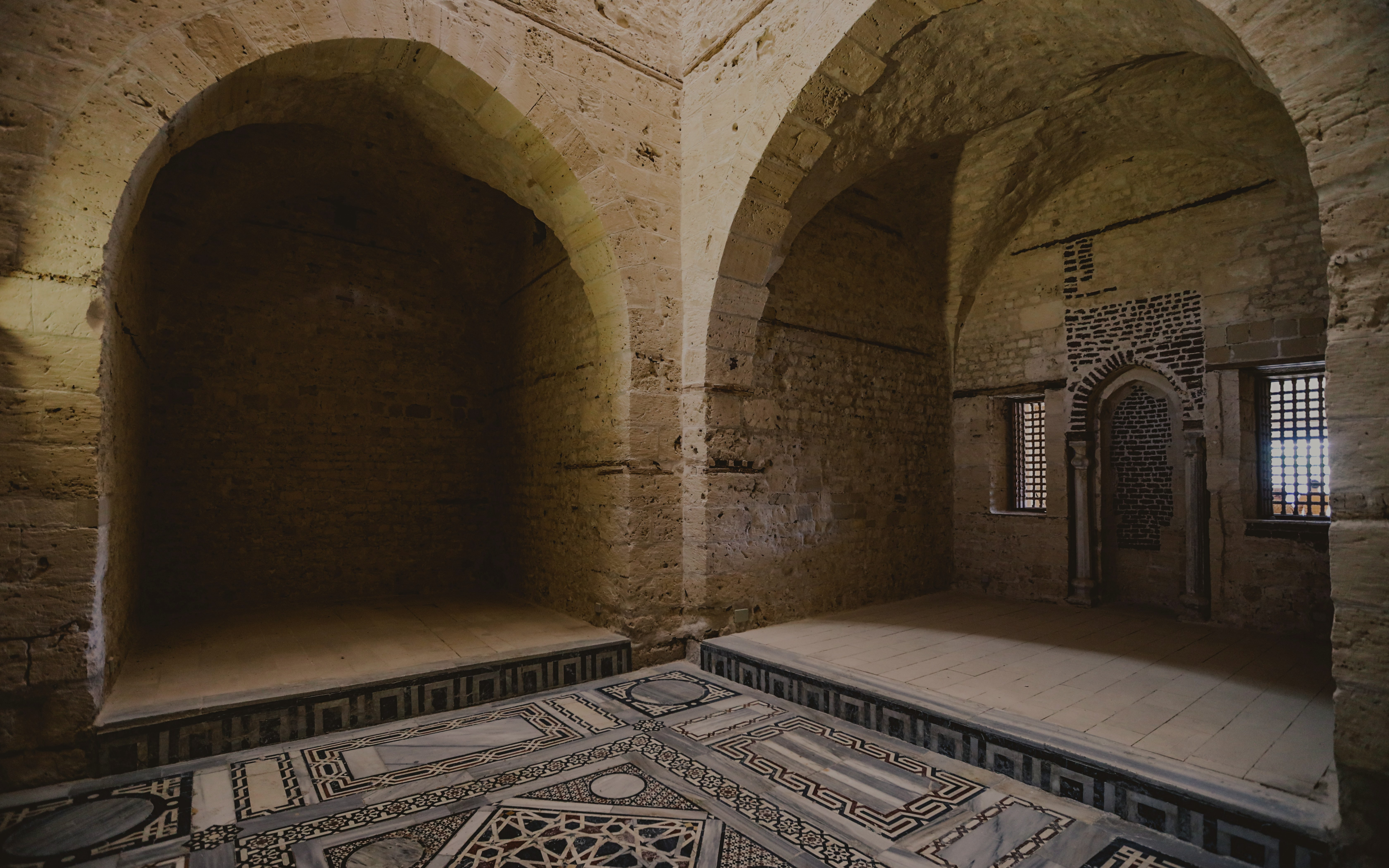 Interior of the mosque inside the Citadel of Qaitbay, Egypt, featuring stone arches and intricate floor patterns.