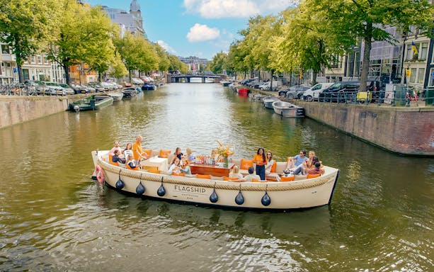 Luxury open boat cruise on Amsterdam canal with passengers enjoying the view.