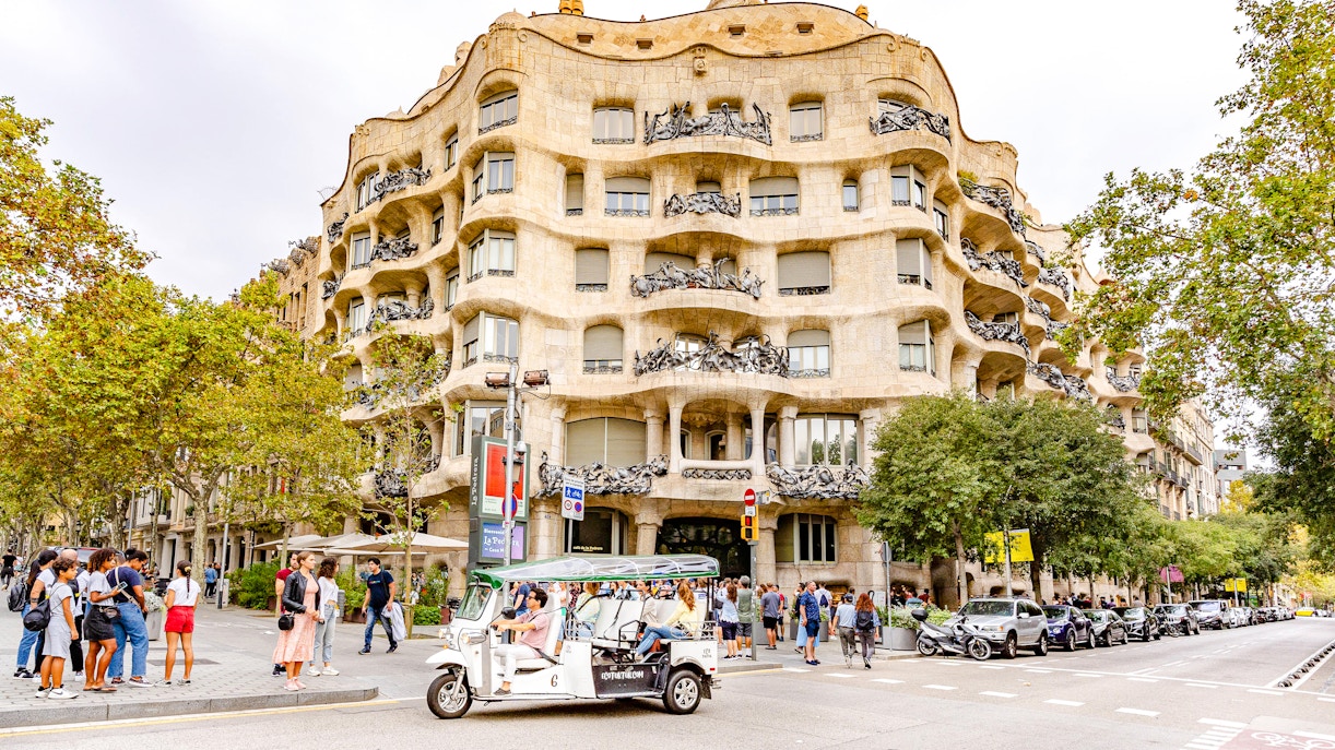Tuk tuk driving past La Pedrera (Casa Mila) in Barcelona.