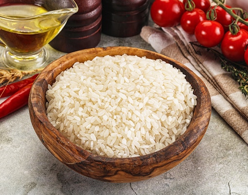 Arborio rice grains in a wooden bowl, essential for authentic Italian risotto.
