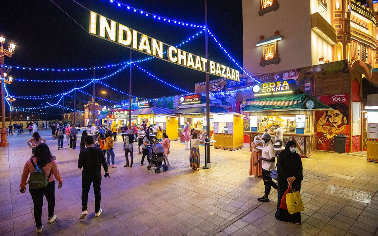 Visitors exploring Indian Chaat Bazaar at Global Village Dubai, with food stalls and vibrant lights.
