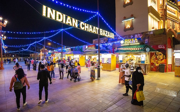 Visitors exploring Indian Chaat Bazaar at Global Village Dubai, with food stalls and vibrant lights.