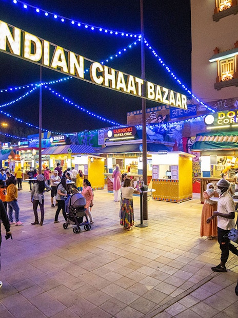 Visitors exploring Indian Chaat Bazaar at Global Village Dubai, with food stalls and vibrant lights.