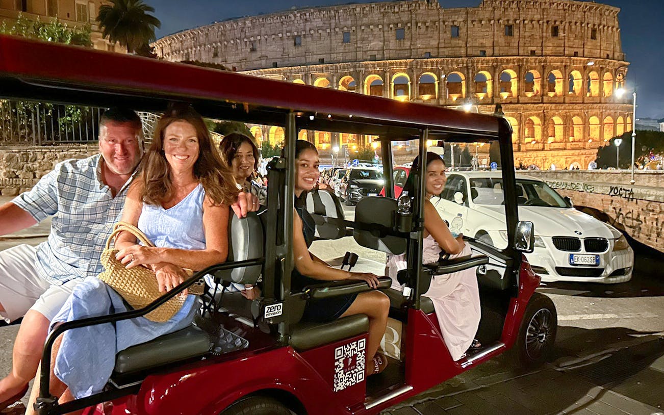 Golf cart driving past illuminated Colosseum during Rome night tour.