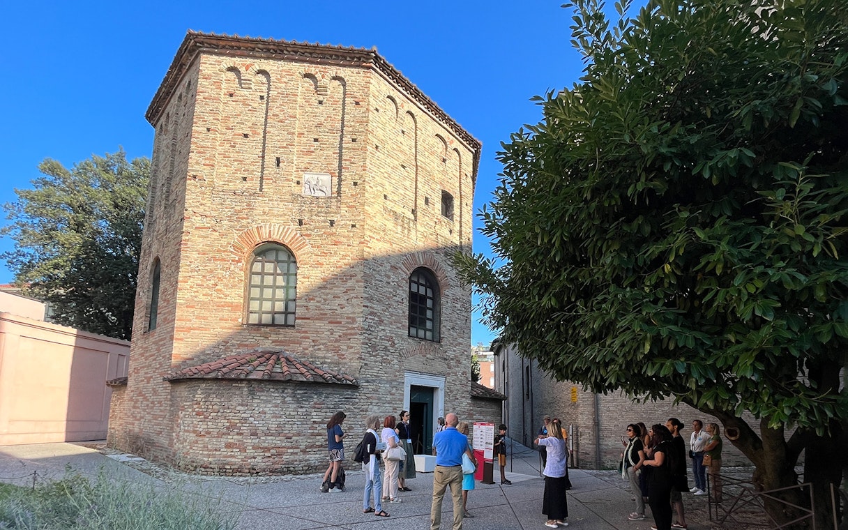 Tour group outside a historic brick building in Ravenna, Italy, during a UNESCO monuments guided tour.
