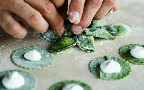 Hands shaping green pasta during a cooking class at an agritourism in Bardolino, Lake Garda.