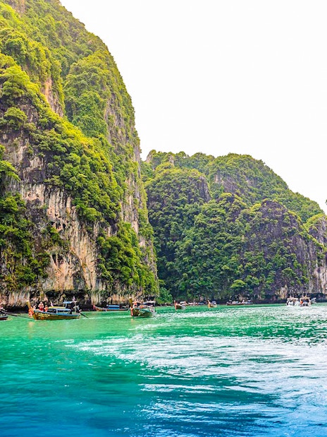 Longtail boats in turquoise waters of Pileh Lagoon, surrounded by limestone cliffs, Krabi.