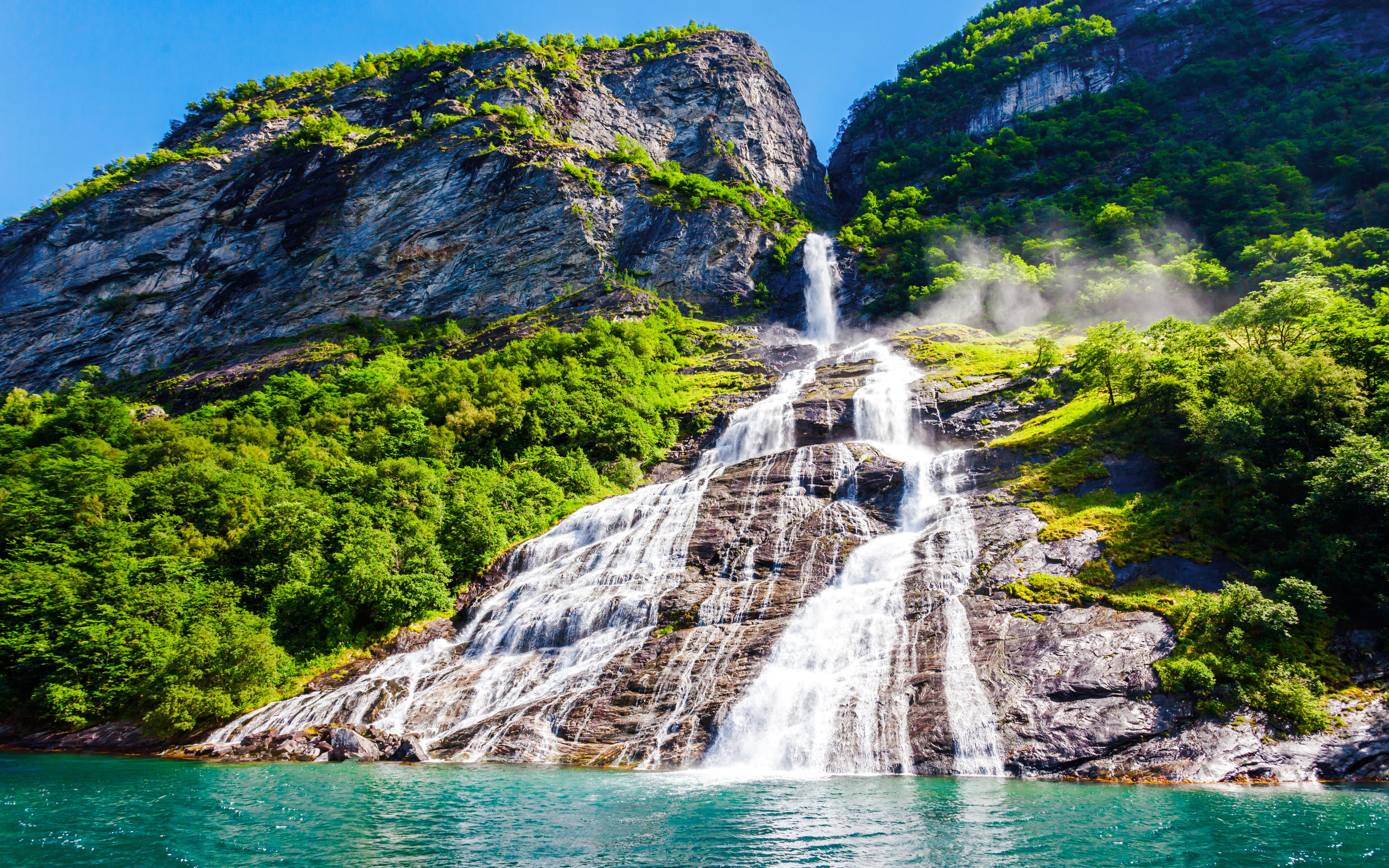 Friaren Waterfall cascading down a rocky cliff surrounded by lush greenery in Geiranger, Norway.