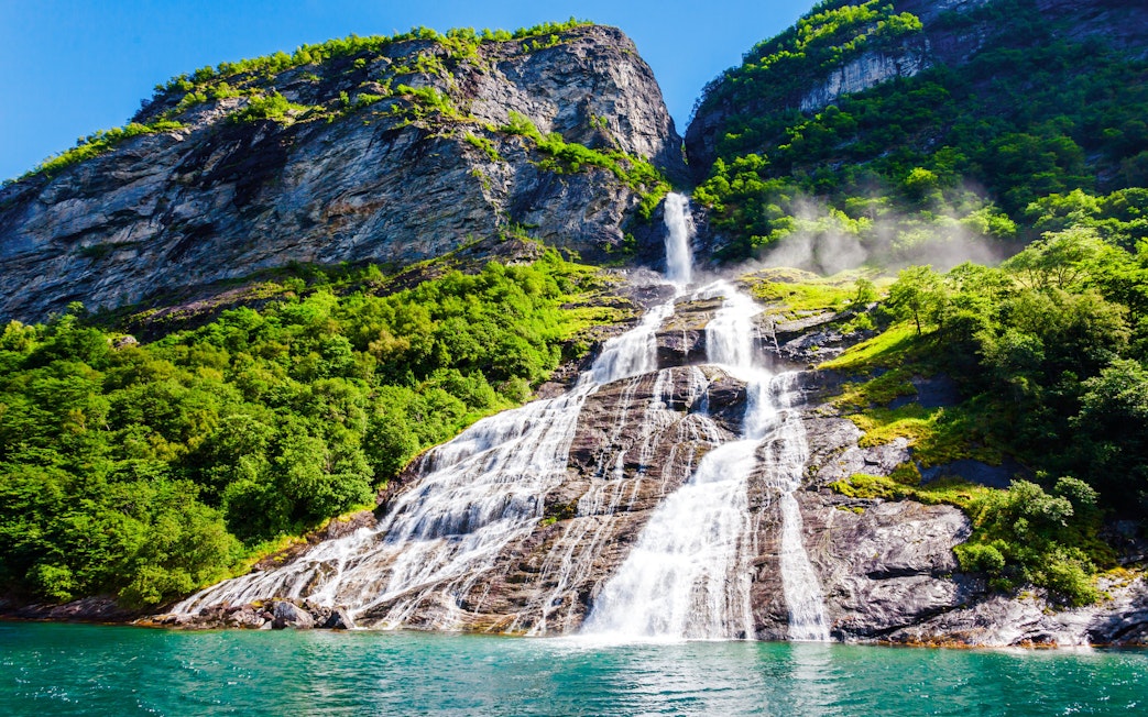Friaren Waterfall cascading down a rocky cliff surrounded by lush greenery in Geiranger, Norway.