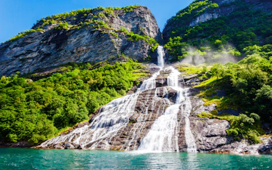 Friaren Waterfall cascading down a rocky cliff surrounded by lush greenery in Geiranger, Norway.