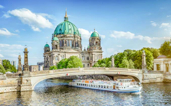 Berliner Dom viewed from a river cruise, with a boat passing under a bridge.