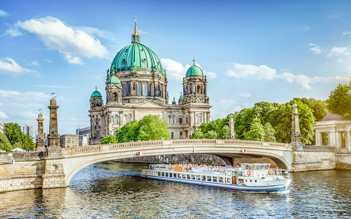 Berliner Dom viewed from a river cruise, with a boat passing under a bridge.