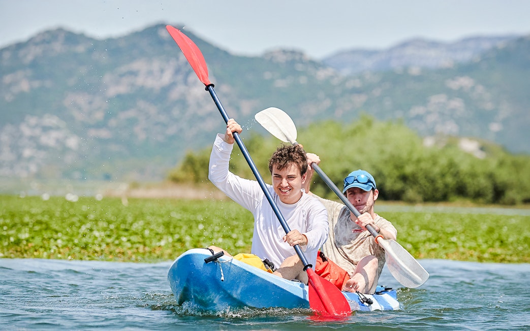 Kayakers paddling on Lake Skadar with mountains in the background.