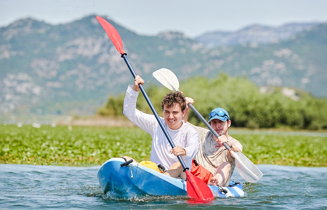 Kayakers paddling on Lake Skadar with mountains in the background.