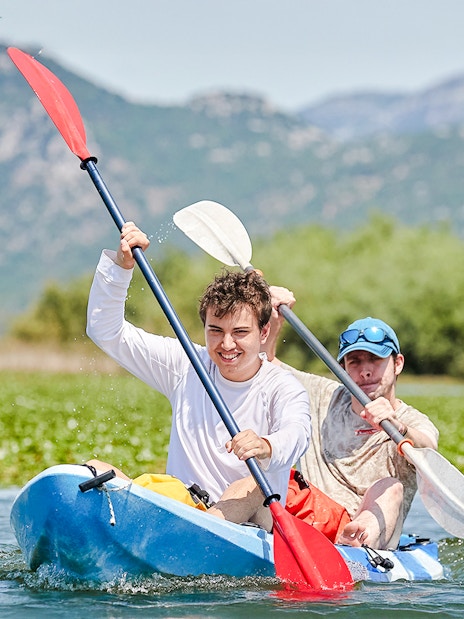 Kayakers paddling on Lake Skadar with mountains in the background.