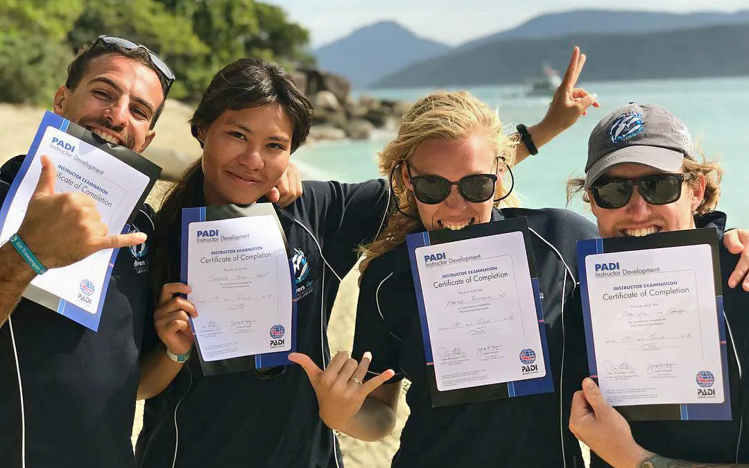 PADI course graduates holding certificates on a beach near the Great Barrier Reef.