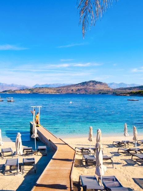 White sand beach with lounge chairs and umbrellas by blue water in Ksamil, Albania.