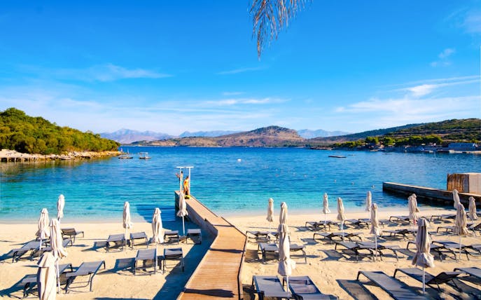 White sand beach with lounge chairs and umbrellas by blue water in Ksamil, Albania.