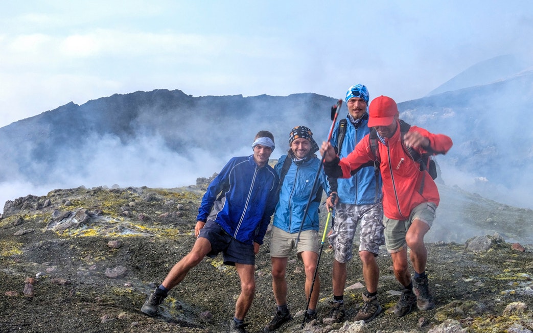 Group hiking on Mount Etna, Catania, with volcanic landscape in the background.