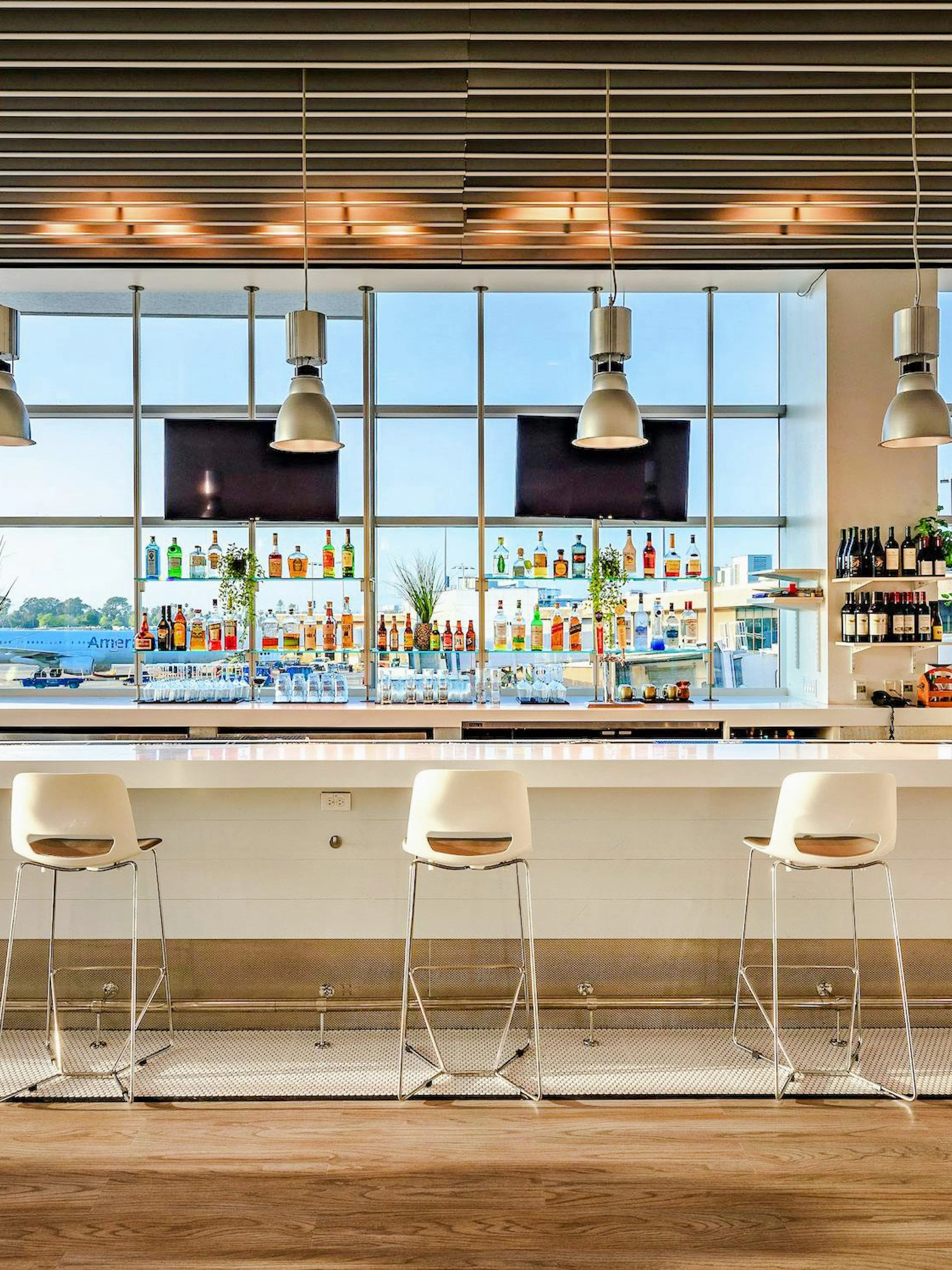 Aspire Lounge bar area with seating and view of runway at San Diego International Airport.
