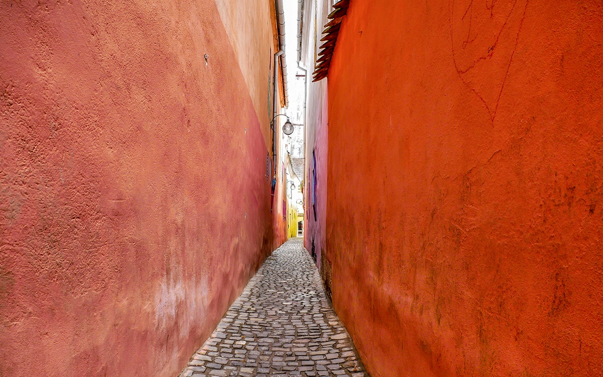 Narrow cobblestone alley of Rope Street, Brasov with colorful walls.