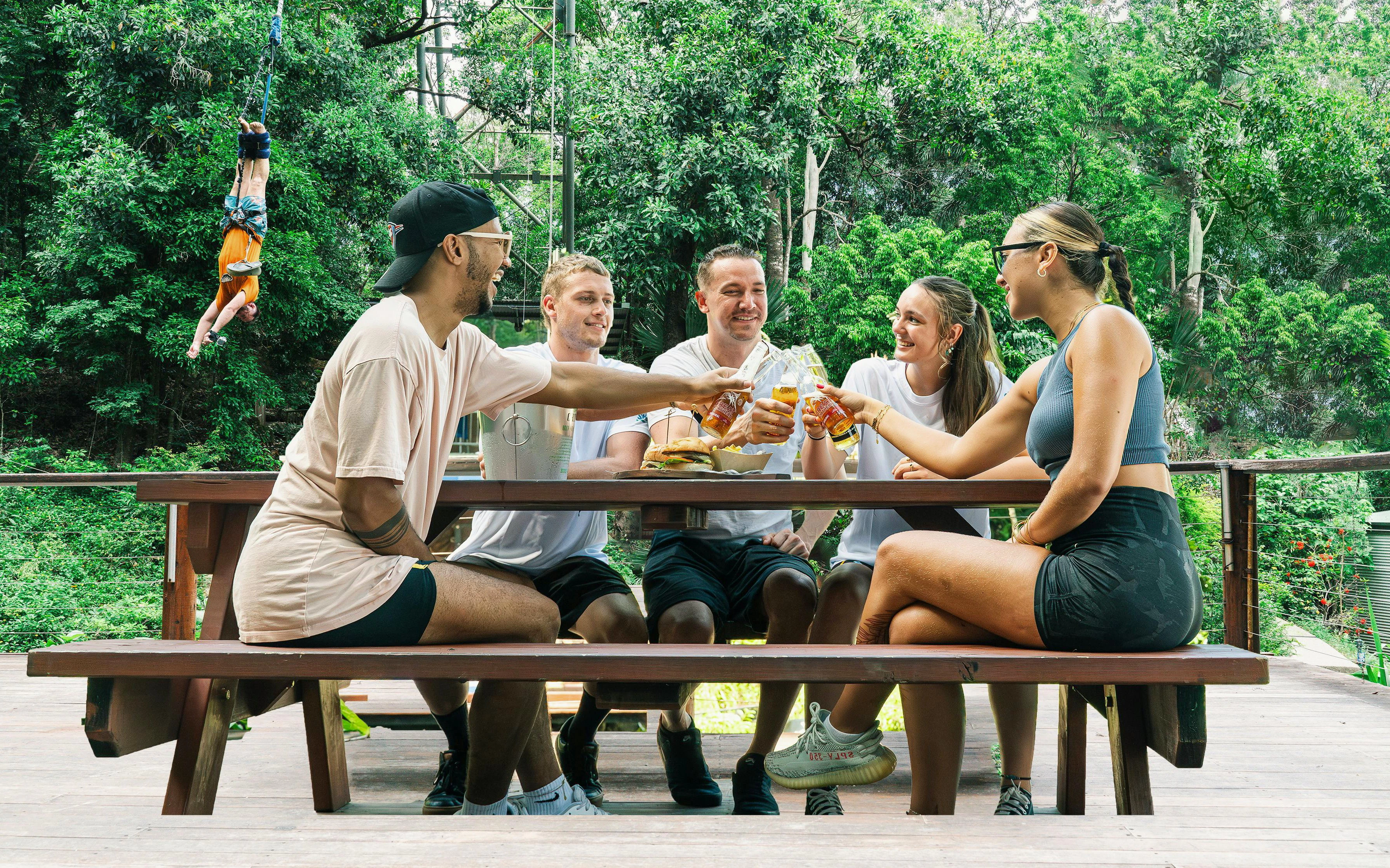 Visitors enjoying lunch at a picnic table in Skypark Cairns with a bungee jumper in the background.