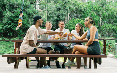 Visitors enjoying lunch at a picnic table in Skypark Cairns with a bungee jumper in the background.