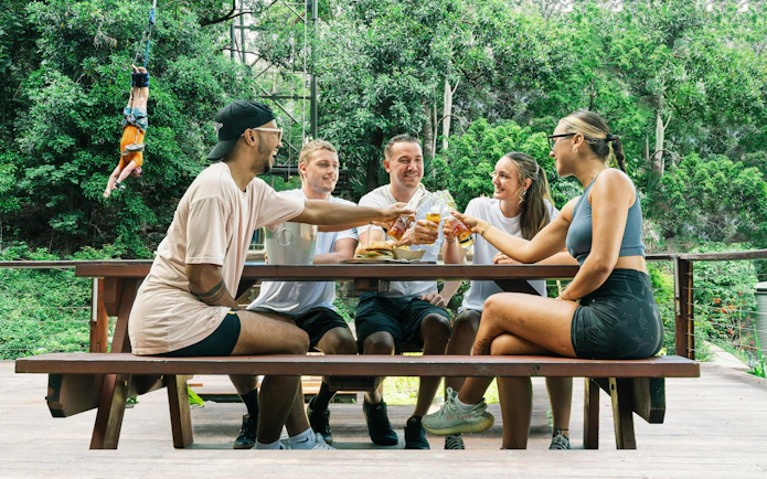 Visitors enjoying lunch at a picnic table in Skypark Cairns with a bungee jumper in the background.