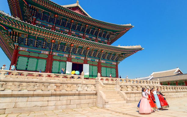Gyeongbokgung Palace in Seoul with visitors in traditional hanbok attire.