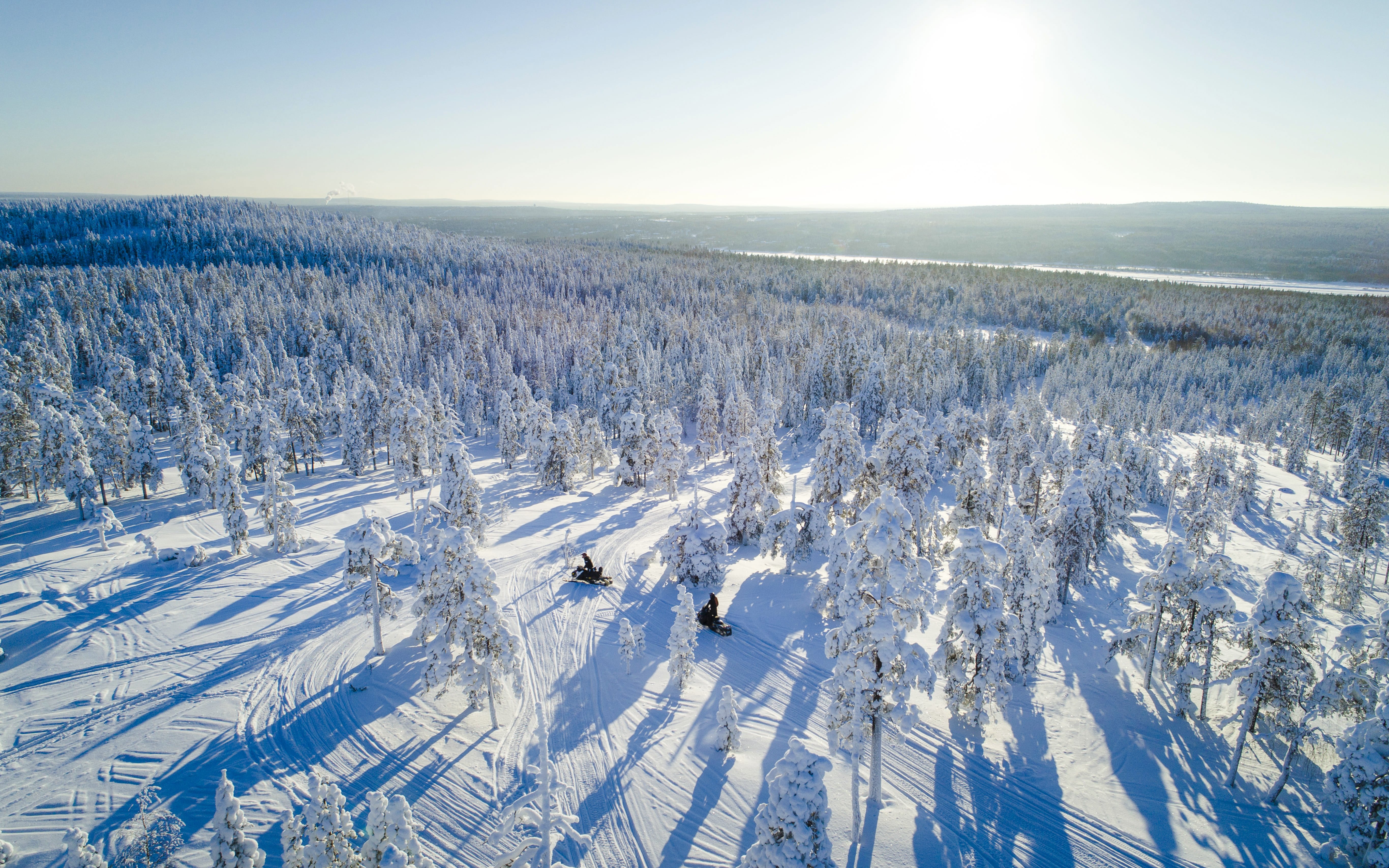 Aerial view of snowmobiles on a snowy trail through a forest near Rovaniemi.