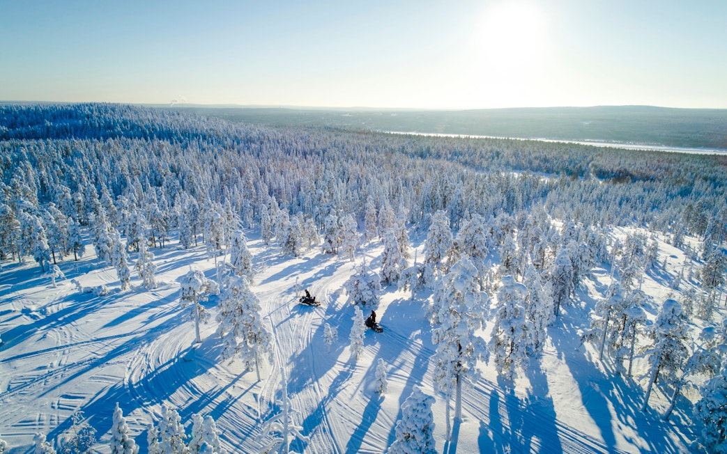 Aerial view of snowmobiles on a snowy trail through a forest near Rovaniemi.