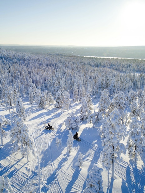 Aerial view of snowmobiles on a snowy trail through a forest near Rovaniemi.