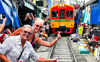 Train passing through Maeklong Railway Market with tourists taking photos, part of the Floating Market & Railway Market tour.