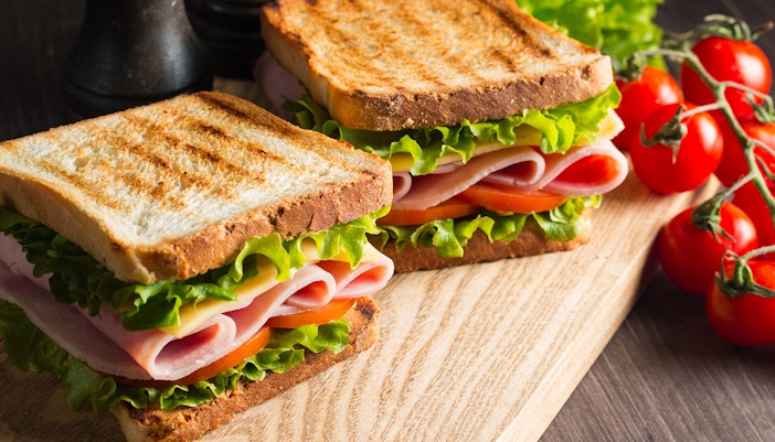 Ham and cheese sandwiches with lettuce and tomato on a wooden board, next to vine tomatoes.
