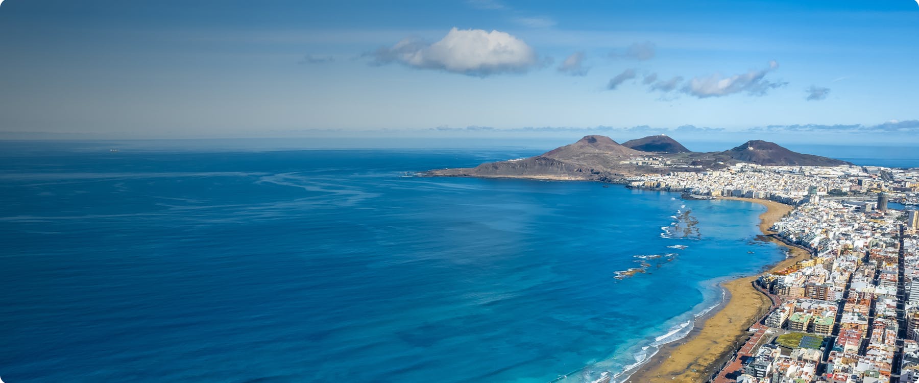 Aerial view of Las Palmas de Gran Canaria coastline with cityscape and mountains.