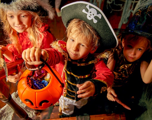 Children in pirate and witch costumes holding a pumpkin bucket filled with candy.