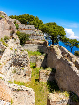 Ancient stone ruins of Villa Jovis on Capri, Italy, with trees and sea in the background.