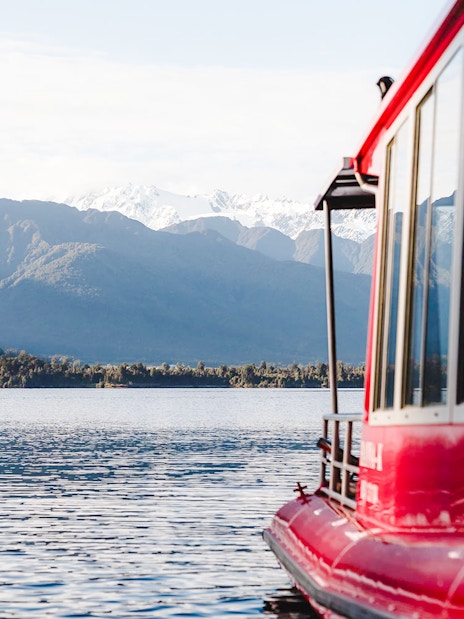 Red boat on a scenic cruise in Franz Josef with mountain backdrop.