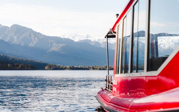 Red boat on a scenic cruise in Franz Josef with mountain backdrop.