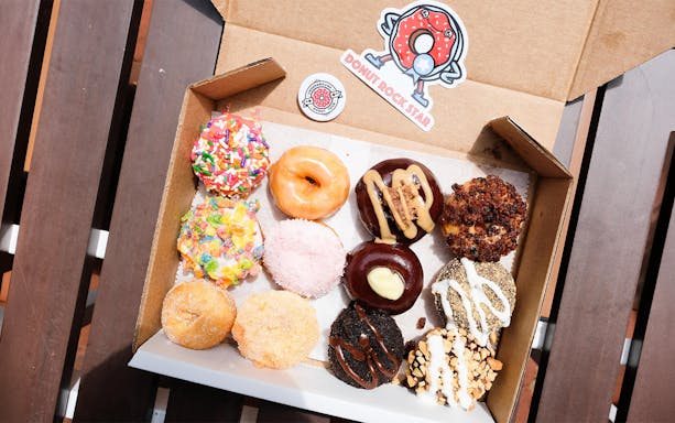 Assorted donuts with various toppings in a box on a wooden table.