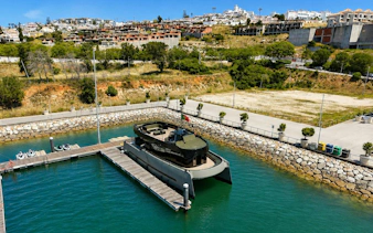 Espirito Oceanico boat docked in a marina with hillside town in the background.
