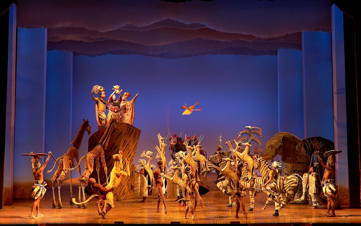 Stage performance of The Lion King with actors in animal costumes.