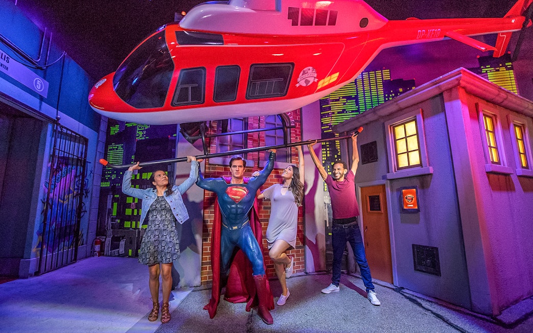 Tourists posing with Superman wax statue holding helicopter at Madame Tussauds.