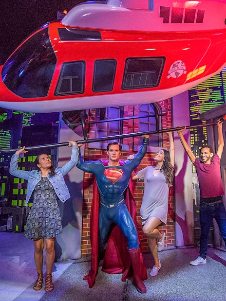 Tourists posing with Superman wax statue holding helicopter at Madame Tussauds.