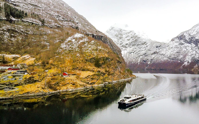 Cruise ship sailing through Geirangerfjord with snow-capped mountains and village in Norway.